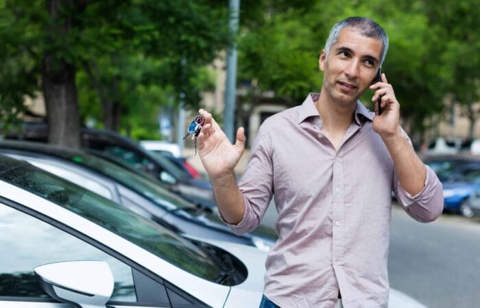 homem fala ao celular ao lado de carro